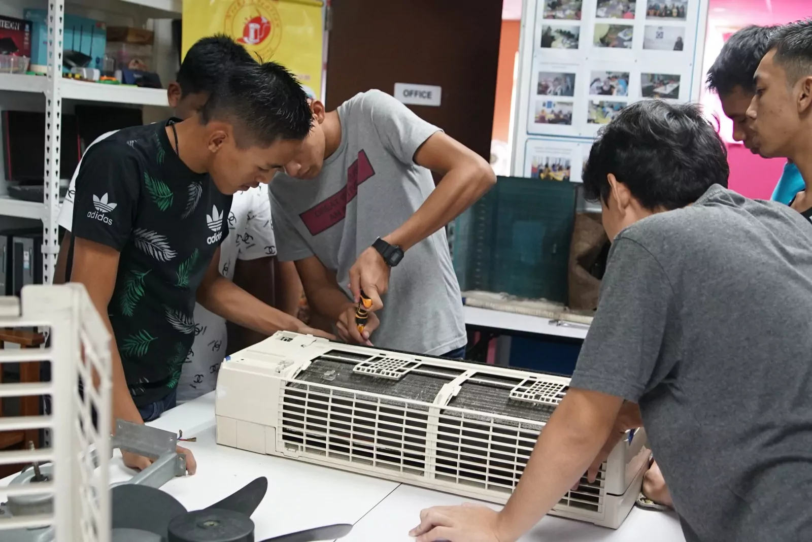 Trainees opening up an air-conditioner unit at the bench