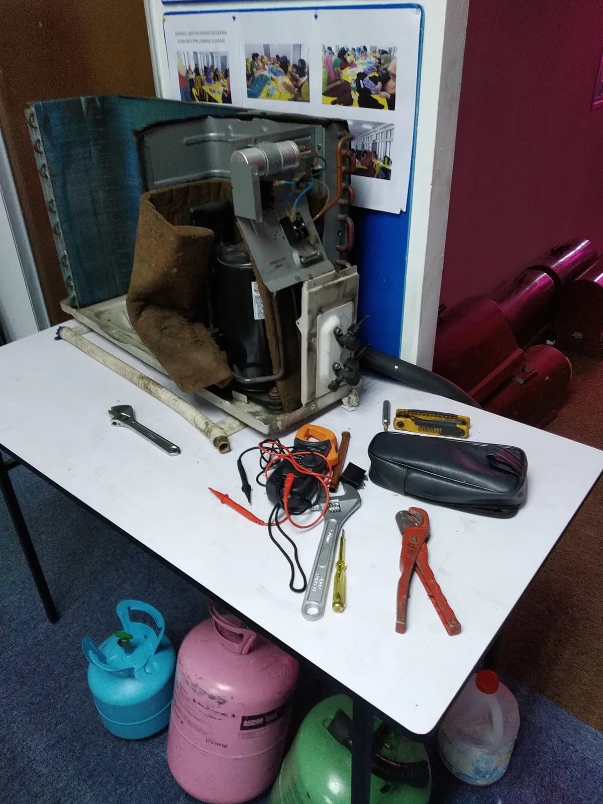 A dismantled unit, meters and hand tools laid out on a repair bench