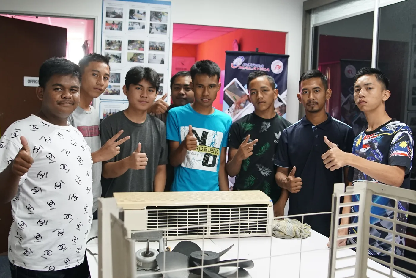 A group of trainees and their instructor gathered around an air-conditioner unit at the workshop